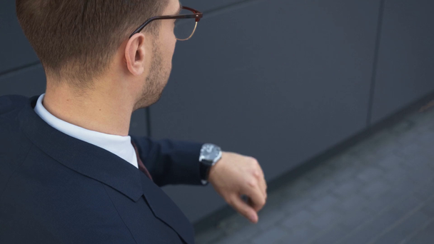 vista trasera del hombre de negocios en gafas mirando el reloj en la mano
 - Imágenes, Vídeo