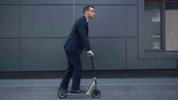 businessman in formal wear riding kick scooter near grey building - Footage, Video