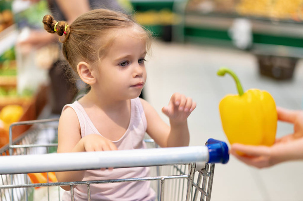 Little Caucasian girl chooses fresh vegetables in the supermarket.  - Фото, изображение