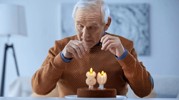 Aufgebrachter Rentner blickt mit Kerzen und berührenden Augen auf Geburtstagstorte  - Filmmaterial, Video