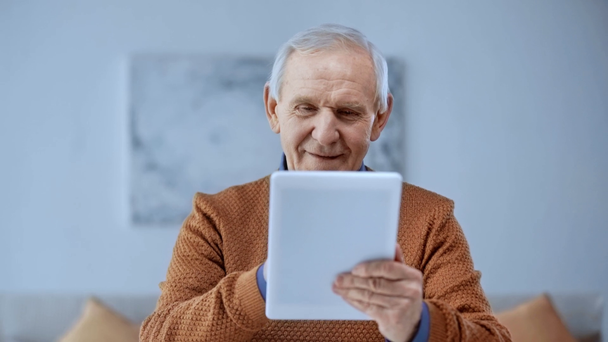 szelektív középpontjában boldog idős férfi segítségével digitális tabletta, és mosolyogva otthon  - Felvétel, videó