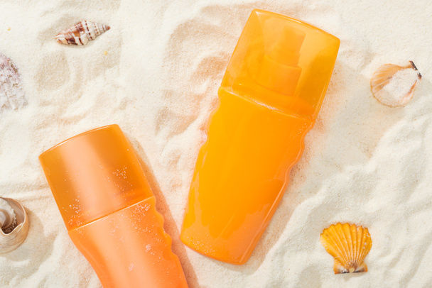 orange bottles of sunscreen on golden sand with seashells - Foto, imagen