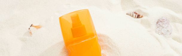 Orangefarbene Flasche Sonnencreme auf Sand mit Muscheln, Panoramaaufnahme - Foto, Bild