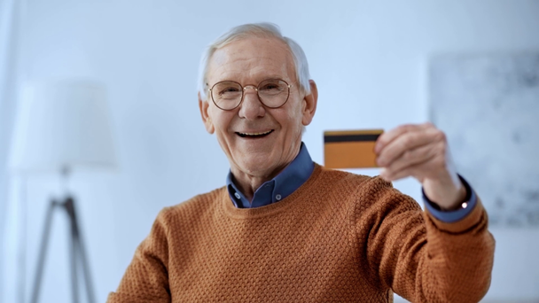 messa a fuoco selettiva di felice uomo anziano in occhiali in possesso di carta di credito e sorridente a casa
  - Filmati, video