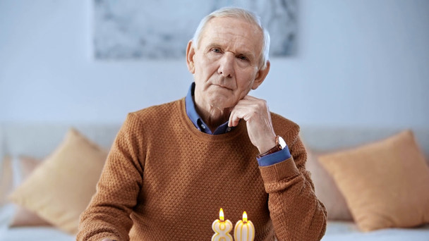 enfoque selectivo de pensionista molesto mirando pastel de cumpleaños con velas en casa
  - Imágenes, Vídeo