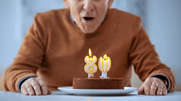 selective focus of senior man blowing burning candles on birthday cake  - Footage, Video