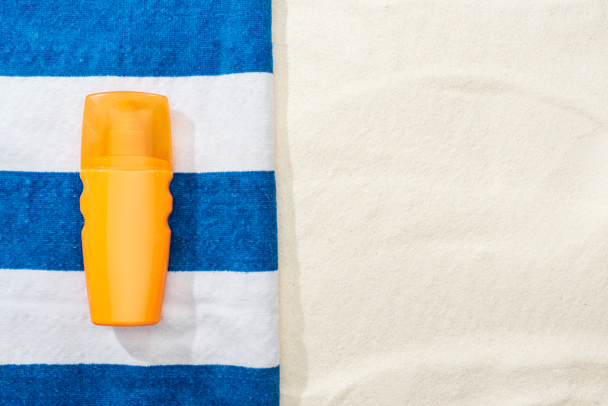 top view of sunscreen and striped blue and white towel on sand - Photo, Image