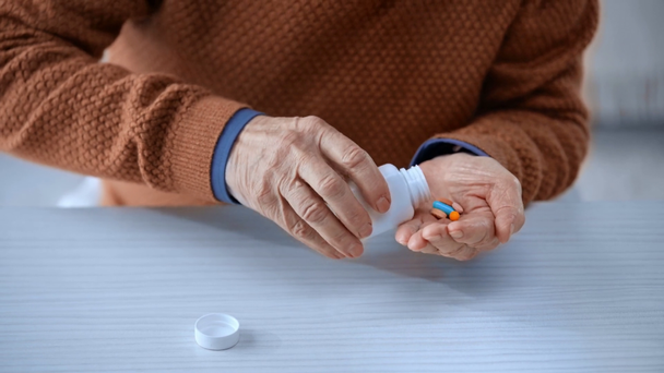 vue recadrée d'un homme âgé prenant une bouteille et mettant des pilules dans une main coupée
  - Séquence, vidéo