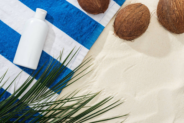 top view of palm leaves, coconuts and striped towel with white sunscreen on sand  - Photo, Image