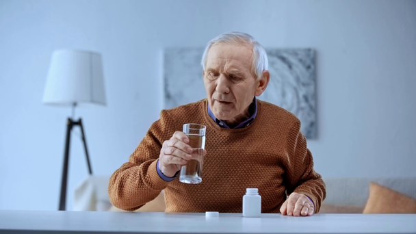 senior man opening bottle, taking medicine and drinking water at home  - Footage, Video