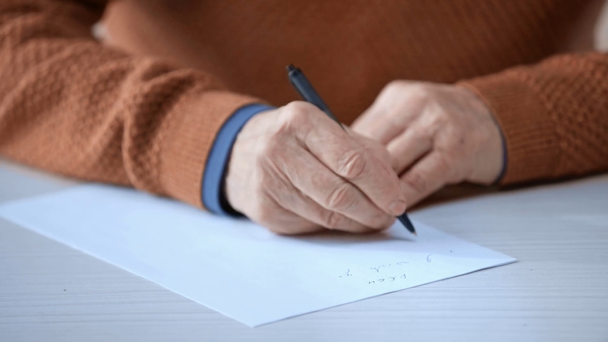 обрізаний вид на старшого чоловіка, який тримає ручку під час написання на папері
  - Кадри, відео