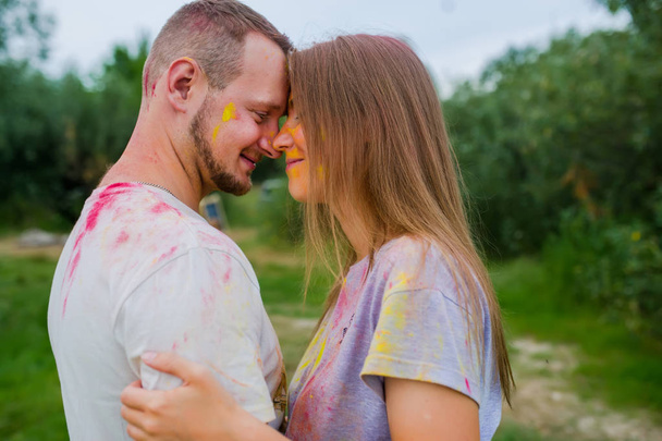 Paar in veelkleurige verven knuffelen in de zomer weide. Zijaanzicht - Foto, afbeelding