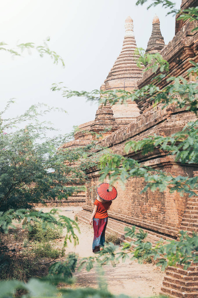Блондинка с красным зонтиком стоит среди храмов и пагод древнего Багана в Мьянме
 - Фото, изображение