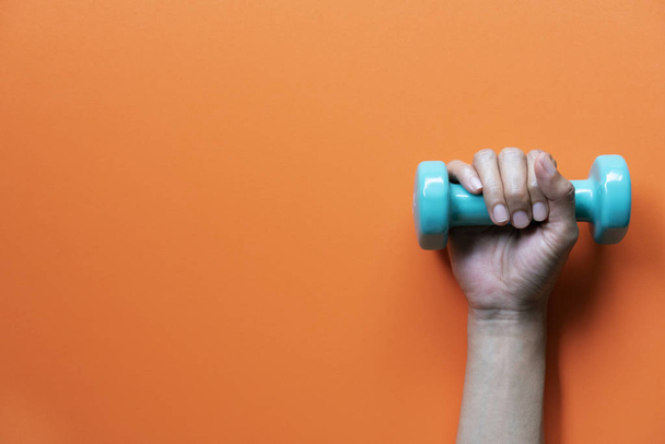 woman hand holding green dumbbell on orange background - Foto, afbeelding