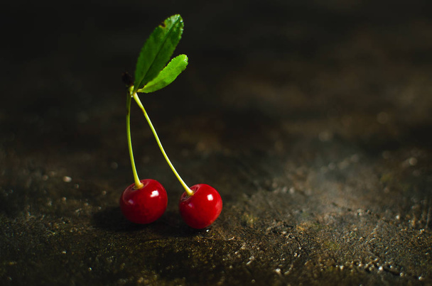 Pair of cherries with green leaves on the old, stone, rustic floor. - Foto, Bild
