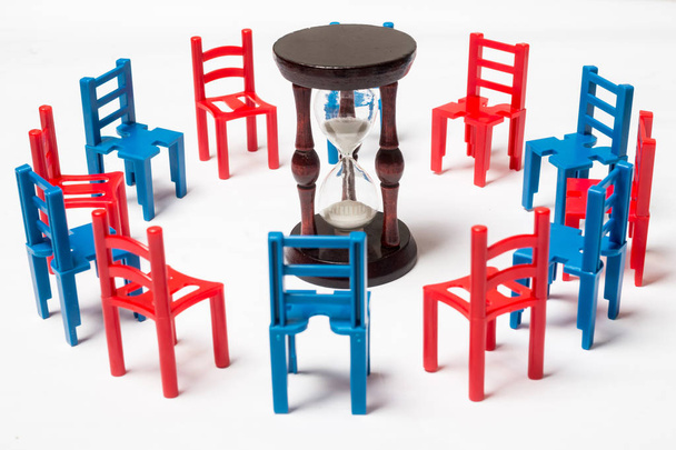 The concept of time management, negotiations, discussion, communication, learning. Multi-colored chairs vacus hourglass on a white background. - Foto, Imagen