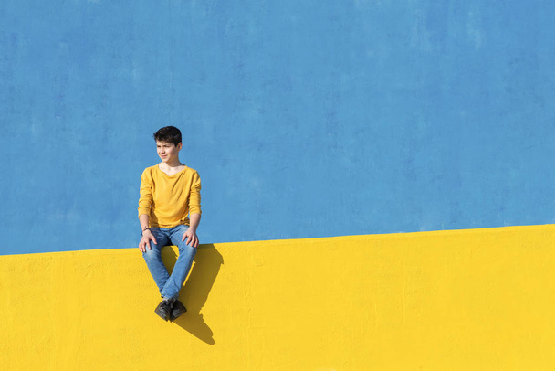 Young boy wearing casual clothes walking against a blue wall in a sunny day - Photo, Image