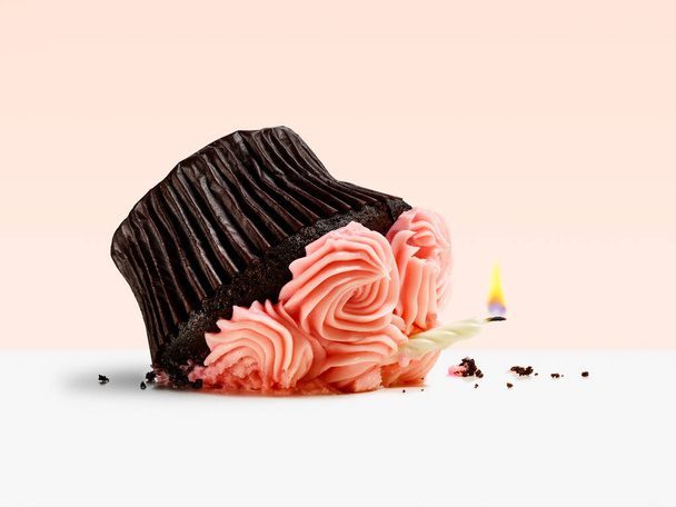 Smashed cupcake with candle flame on a pink background - Photo, Image