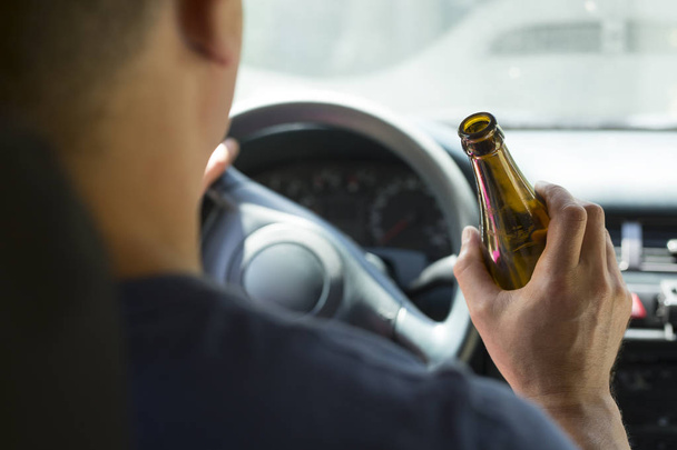 Ο οδηγός κρατά ένα μπουκάλι αλκοολούχο ποτό ενώ οδηγεί ένα αυτοκίνητο. - Φωτογραφία, εικόνα