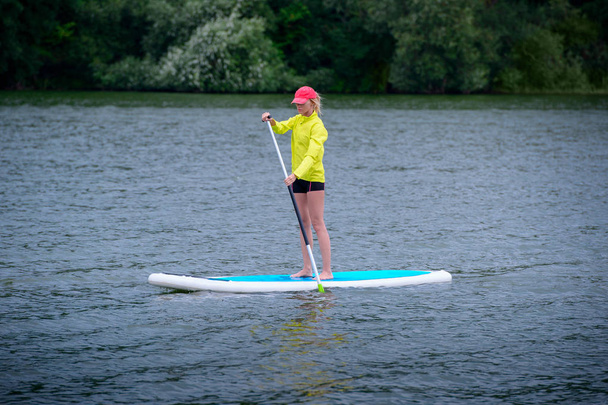 A woman is floating on a SUP board along a large river. Stand on - 写真・画像