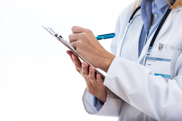 Жінка-лікар заповнює медичну форму в кишені, стоячи прямо над білим тлом
. - Фото, зображення