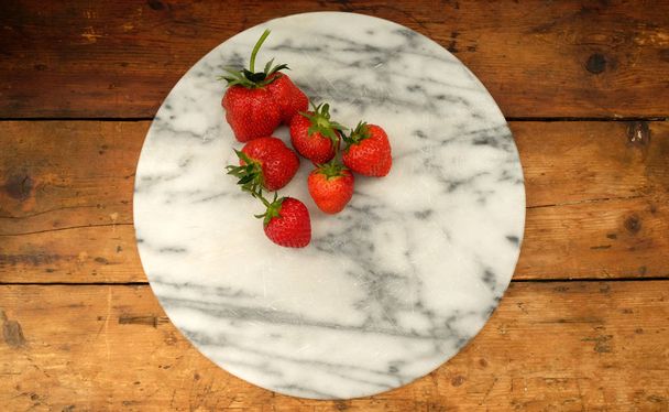 cinco morangos maduros vermelhos em uma placa circular de mármore
  - Foto, Imagem