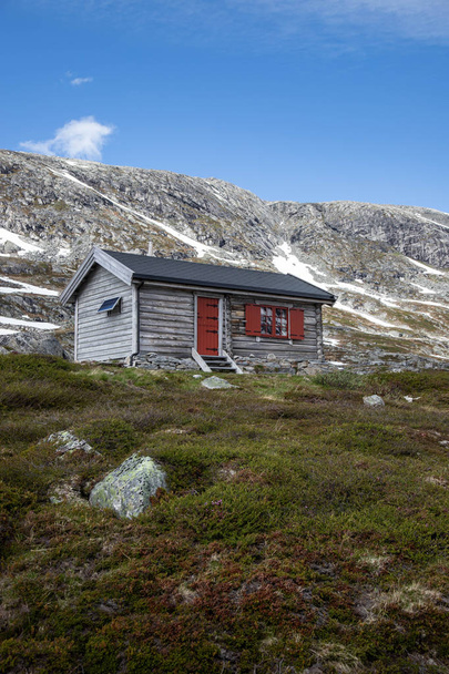 festői kilátás a szürke ház a zöld dombon, hóval borított hegycsúcsok a háttérben, Strynefjellet, Norvégia  - Fotó, kép