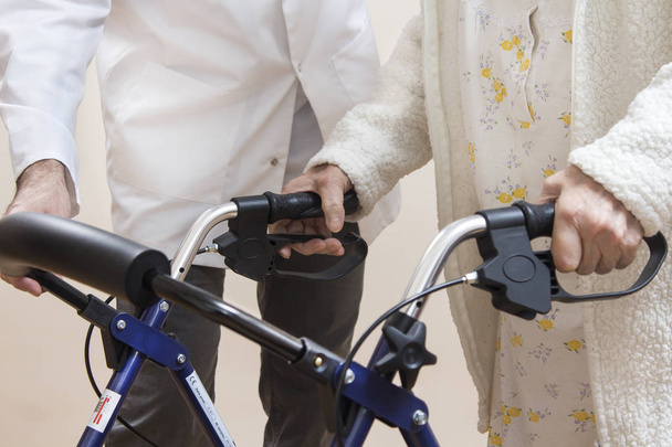Ruce velmi staré ženy drží držadla rehabilitačního chodce. Muž, který si dělá chůvu, pomáhá při chůzi. - Fotografie, Obrázek