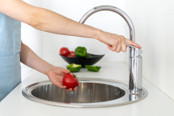 Woman standing on white kitchen and washing tomato in sink - Foto, Imagen