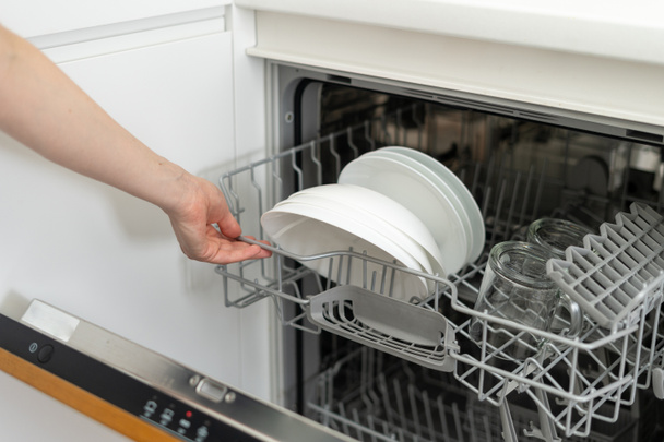 Frau öffnet moderne Geschirrspülmaschine mit Tellern und Tassen, steht auf Küche  - Foto, Bild