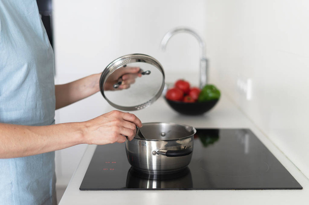 Woman cooking food in saucepan, using built in electric stove - Zdjęcie, obraz