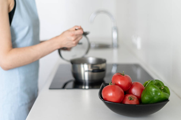 Bowl with vegetables on blurred background with woman cooking food, using electric stove - Foto, immagini