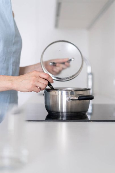 Woman cooking food in saucepan, using built in electric stove - Photo, Image