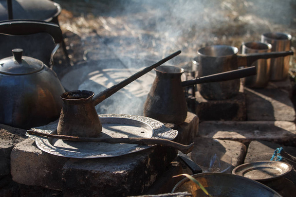 Крупный план нескольких копченых цезава на костре для кофе, чайник и сковородка, концепция приготовления пищи на природе
 - Фото, изображение