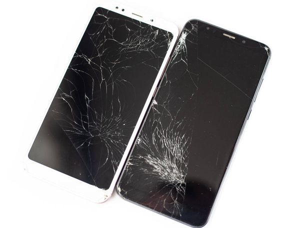 twee gebroken telefoons van wit en zwart op een witte achtergrond. gebarsten touchscreen-glas van het aanraakscherm isolaat - Foto, afbeelding