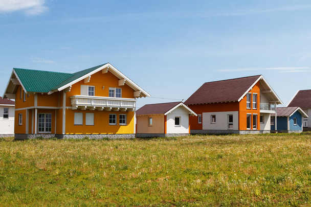 moderne kleine gekleurde huizen gebouwd op het platteland tegen een blauwe hemel met wolken. - Foto, afbeelding