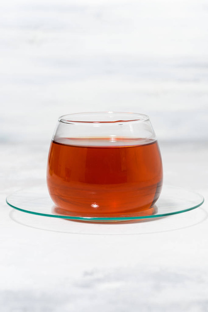 скляна чашка ароматного чаю на білому фоні, вертикальна
 - Фото, зображення