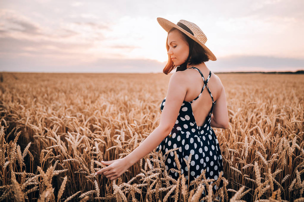 Woman in retro style dress and hat posing in wheat golden field. Travel, harvest, nature, old fashion concept. - Фото, зображення