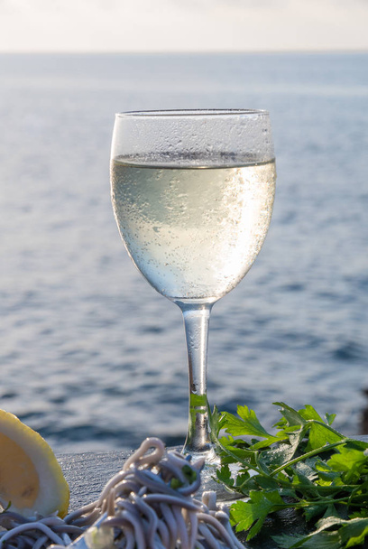 Крупный план бокала вина и северного гуляша, взятого в вилку - приготовленные угри в сопровождении лимона, букет сельдерея на каменном столе - типичное испанское блюдо
 - Фото, изображение