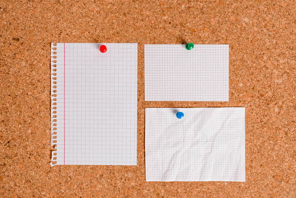 Corkboard with different color and size papers fixed by a pin. Rectangle and square shaped sheets stuck on a billboard by colored thumbtacks. Notice board with empty reminder note. - Photo, image