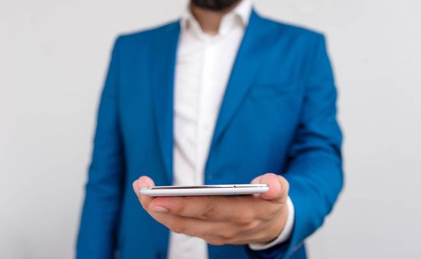 Businessman holds lap top in his hand. Business concept with man holding mobile phone with touch screen. Businessman in blue suite stands with mobile phone in hands. - Photo, Image