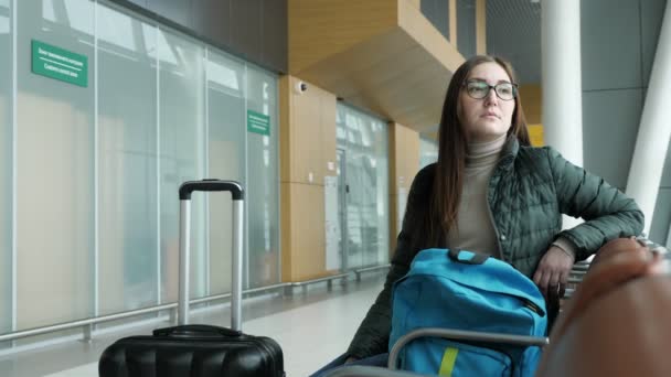 Mladá žena v brýlích čeká na svůj let na letišti v hale.. - Záběry, video