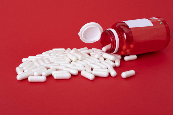 Белые кальциевые таблетки, выливающиеся из красной бутылки на красную заднюю группу
 - Фото, изображение