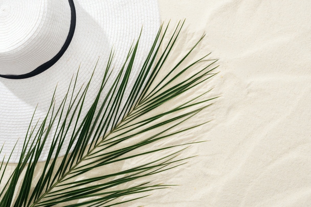 top view of white straw hat and green palm leaf on sand - Φωτογραφία, εικόνα