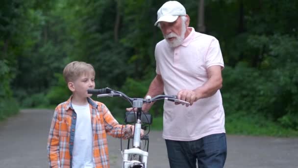 Happy grandfather teaching boy how to ride bicycle at summer park. family, generation, safety and people concept - Footage, Video