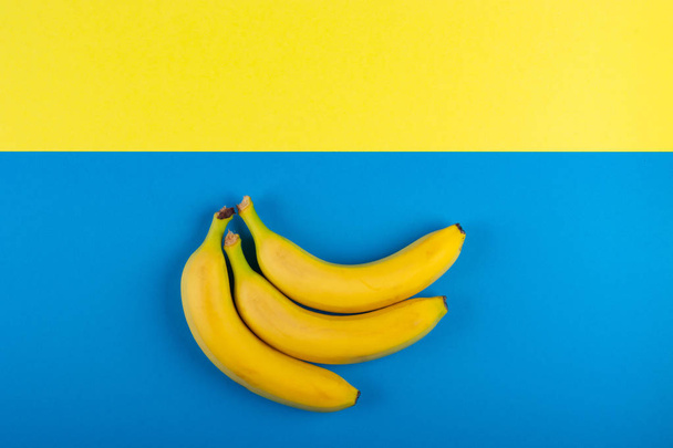 黄色と青の背景に熟したバナナのクローズアップ。ミニマリズム、テキスト用スペース、トップビュー、フラットレイ、コピースペース. - 写真・画像
