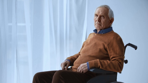Senior behinderter Mann sitzt im Rollstuhl und blickt in Kamera  - Filmmaterial, Video