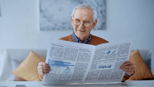 foco seletivo de homem aposentado feliz sentado no sofá e ler jornal em casa
  - Filmagem, Vídeo