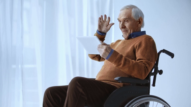 cheerful senior and disabled man holding digital tablet, gesturing then looking at camera while having video call - Footage, Video