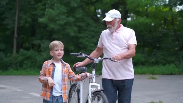 Szczęśliwy dziadek uczy chłopca, jak jeździć na rowerze w letnim parku. Rodzina, pokolenie, bezpieczeństwo i koncepcja ludzi - Materiał filmowy, wideo